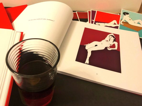 Aufgeschlagene Bücher der limitierten Auflage des Buche Halbvoll oder hlalbleer liegen auf dem Tisch, ein halb volles Glas Rotwein, Postkarten.